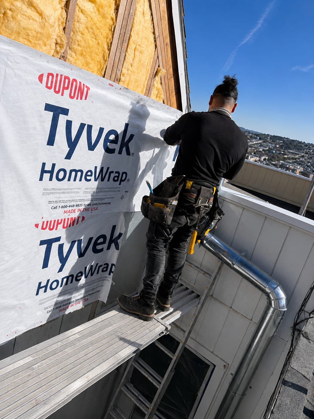 RS Professional Painting crew member installing Tyvek HomeWrap on a Potrero Hill rooftop with the SF skyline in background