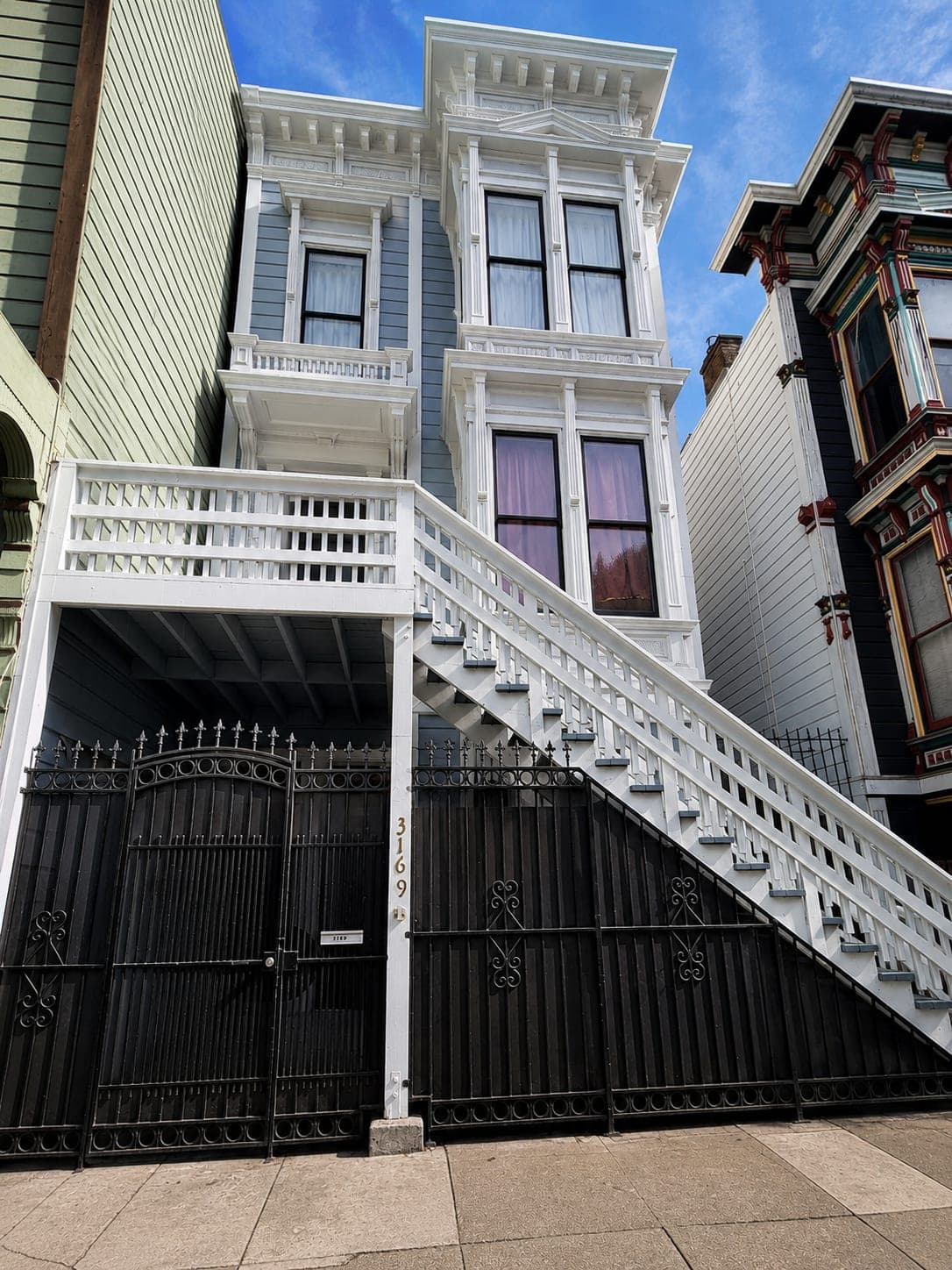 Restored white Italianate Victorian with wrought-iron gate
