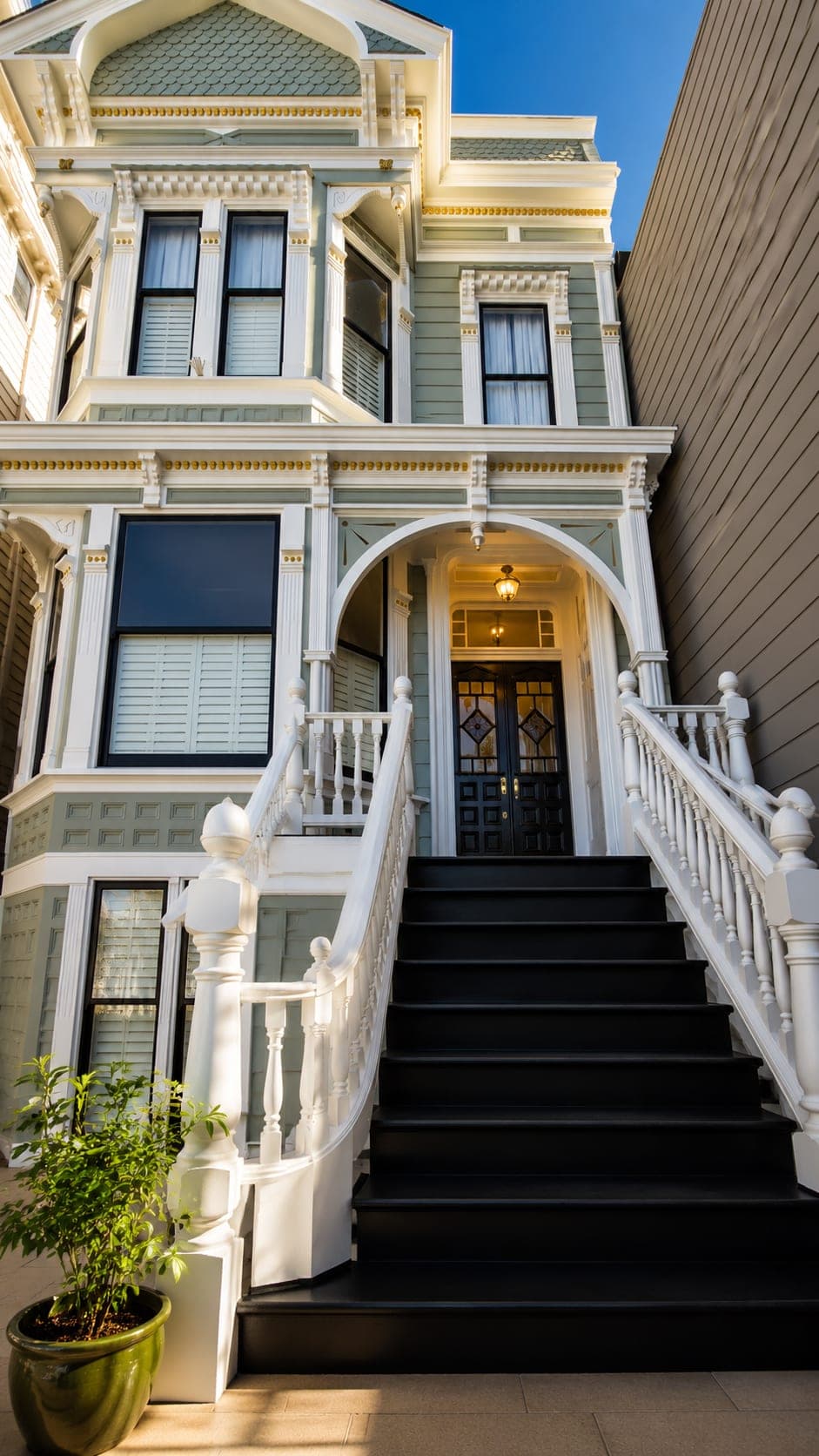 Close-up of the restored entry archway and white balustrade on a sage-green Victorian